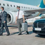 Luxury chauffeur service from JFK Airport – professional driver assisting business traveler with luggage near private car.